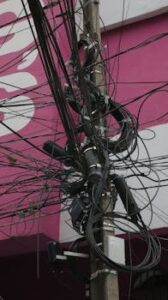 A complex network of tangled power cables on an electric pole in a urban area.