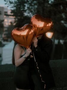 A couple holding heart-shaped balloons embracing in an outdoor setting with a romantic vibe.