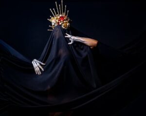 A dramatic portrait featuring a person with a gold headdress and black veil, set against a dark background.