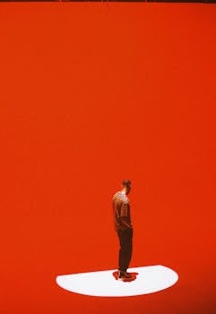 A man stands thoughtfully in a red studio, creating a striking visual contrast.
