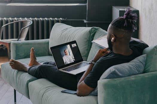 African American man relaxes on a couch while video chatting on a laptop, enjoying a casual day indoors.