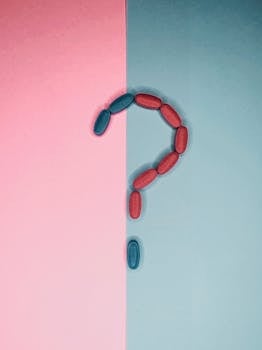 Creative arrangement of red and blue pills forming a question mark on split pink and blue background.