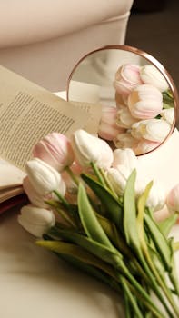 Serene display of white and pink tulips beside an open book and mirror.