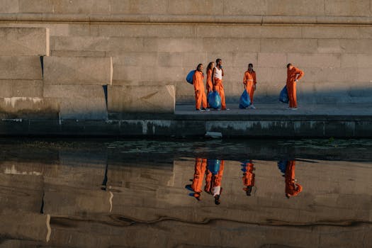 Volunteers in orange uniforms collect trash by the river during an early morning cleanup effort.