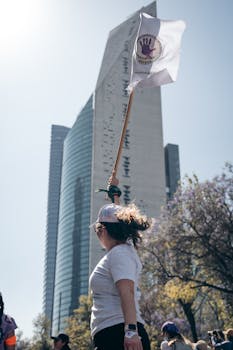 Woman holding a protest flag near a skyscraper in Mexico City, showcasing urban activism.