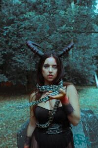 Woman in fantasy costume holding snake in lush forest, evoking mystery.